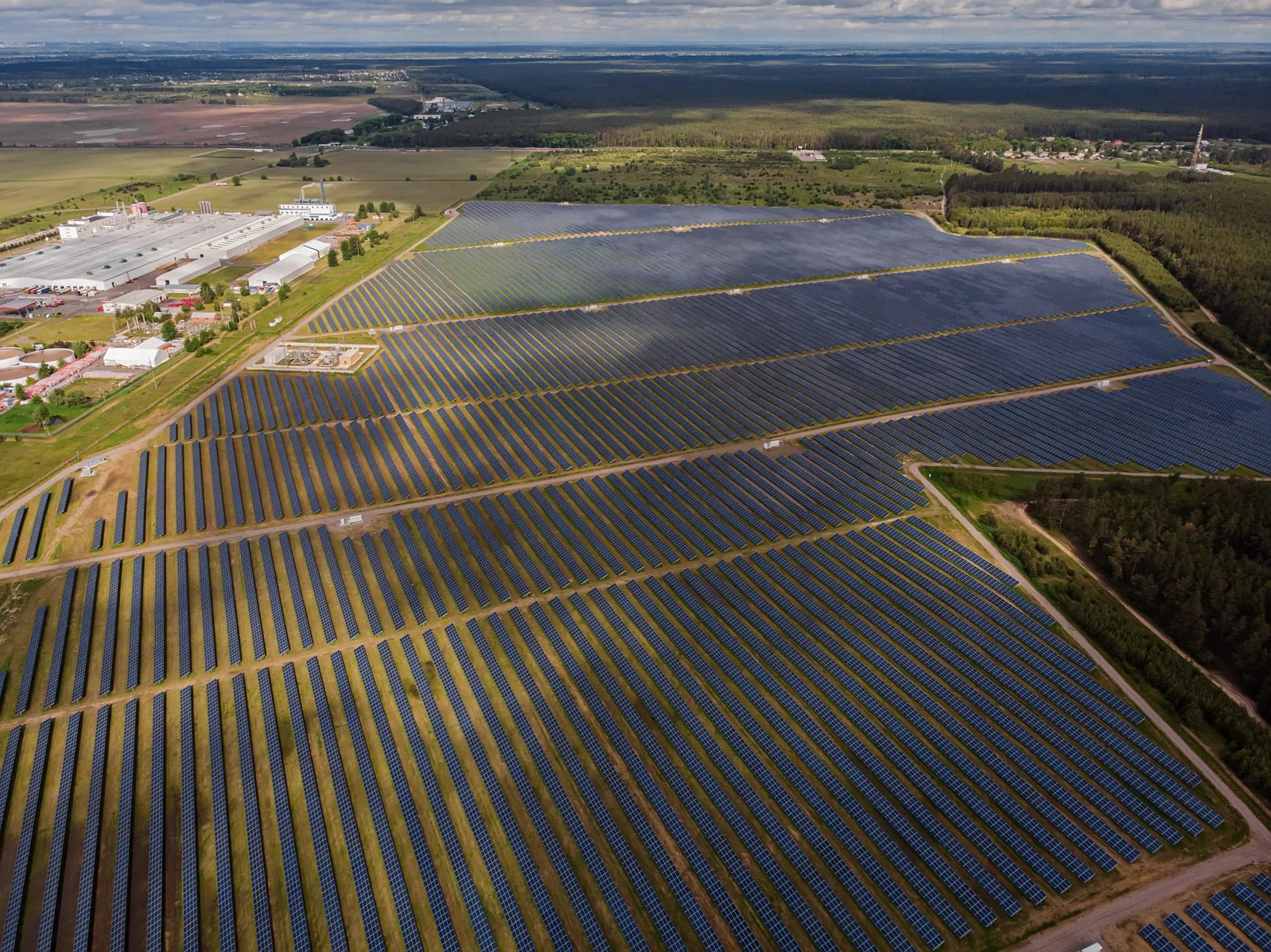 Aerial view of a solar park beside an industrial plant and farmland